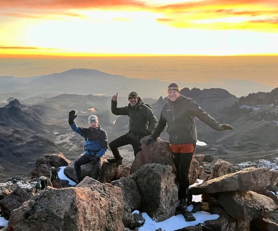 Three friends posing on Mt Kenya Pt Lenana’s snowcapped peak at sunrise Mt Kenya corporate retreat