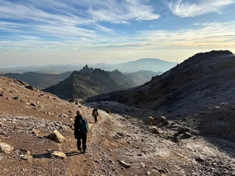 Two mountain climbers trekking Mount Kenya’s alpine snowcapped desert on a sunny day.