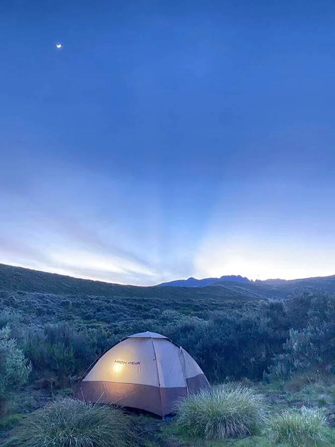 A camp tent with a shining light inside on the slopes of Mount Kenya close to dusk. Peak ahead.