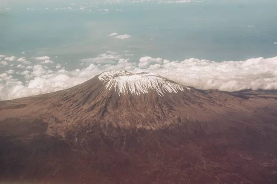 A grand aerial shot of Mount Kilimanjaro, piercing the clouds and snowcapped summit reached 