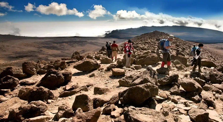 Hikers on a Mt Kilimanjaro climbing tour trekking through a rocky ridge above plains on a sunny day.