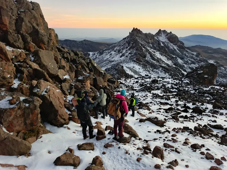 Hikers on the snowcapped peak of Mount Kenya at golden hour carrying bags and climbing gear