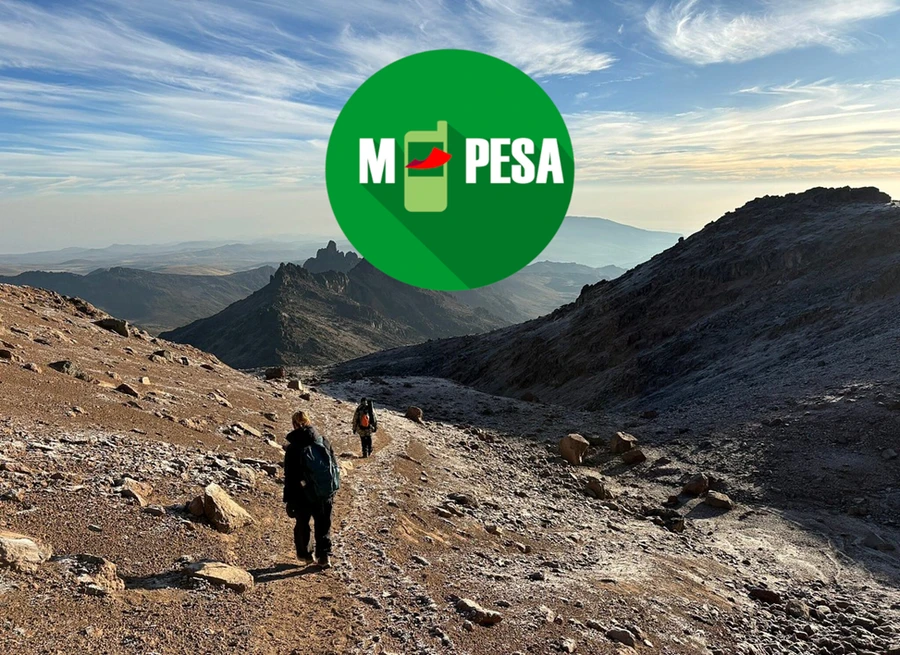 Two hikers trekking Mount Kenya’s rugged, snowcapped landscape on a sunny day. Mpesa logo at the top