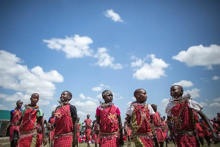 A group of Maasai school children in traditional attire performing a cultural dance on a sunny day