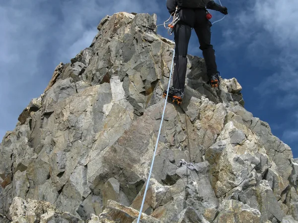 A mountain climber rock climbing Mount Kenya Batian with gear like ropes, anchors, and crampons.