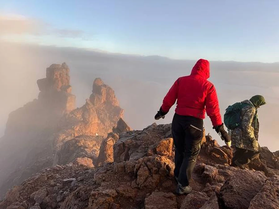 Mount Kenya trekker and guide navigating a rocky section of the mountain under a clear blue sky