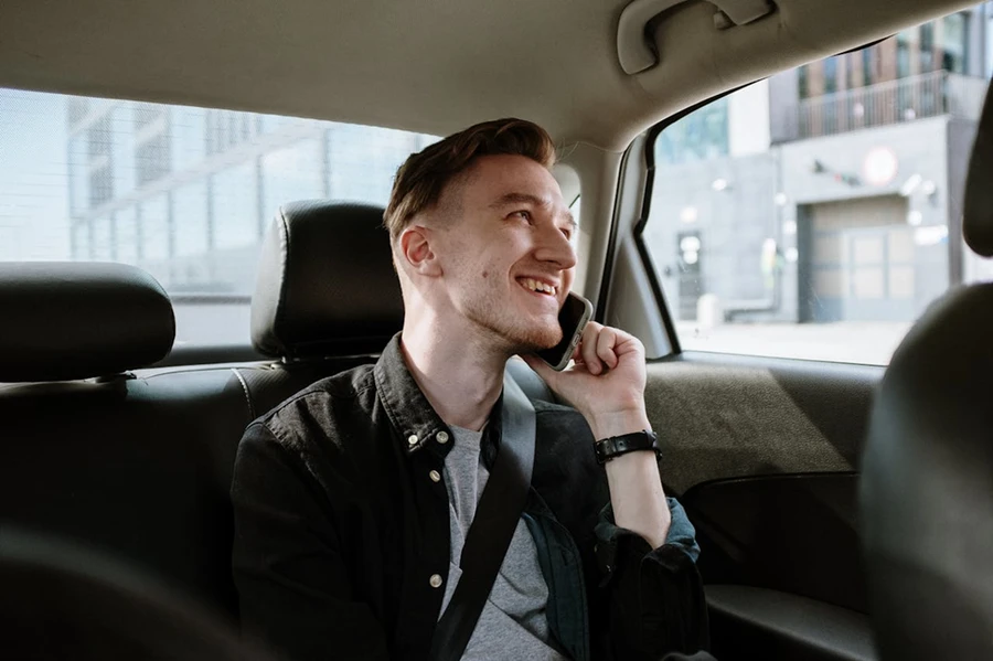 A male passenger in the backseat of an airport transfer cab talking and smiling on the phone