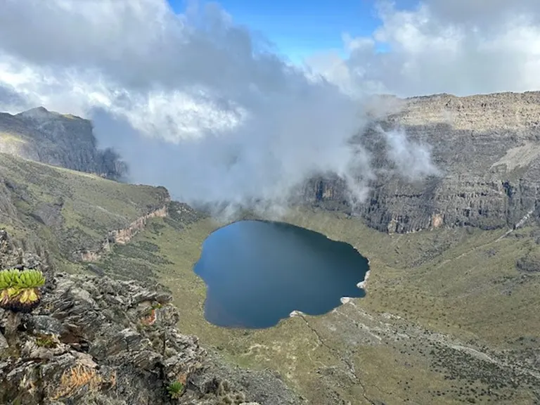 Lake Michaelson on Mt Kenya, surrounded by jagged cliffs and alpine vegetation, partly cloudy day