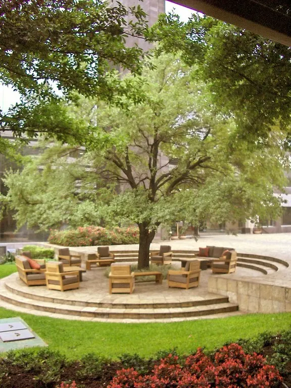 Circular outdoor seating with cushioned chairs around a tree, set in a landscaped garden