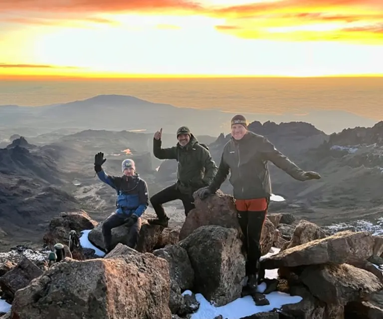 Three friends posing on Mt Kenya Pt Lenana’s snowcapped peak at sunrise Mt Kenya corporate retreat
