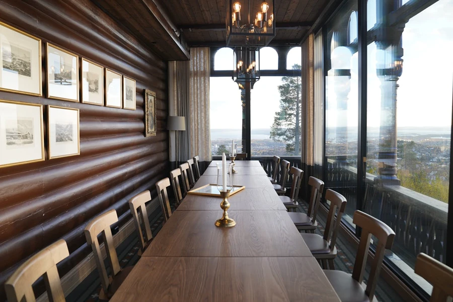 A large conference table in a hall with candle stands and glass windows, natural landscapes outside
