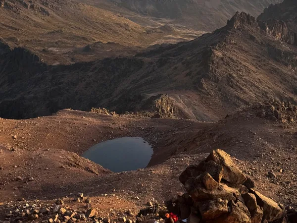 Tourists on a Mount Kenya trek hiking through vast rugged terrain and passing Lake Michaelson