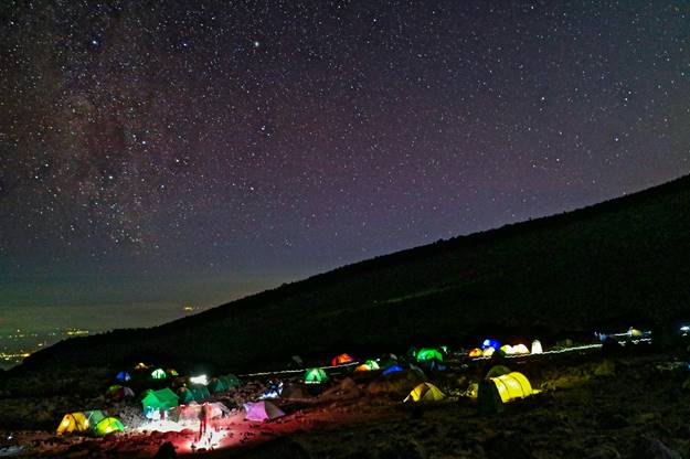 Big campsite with illuminated tents on a mountain slope. A cloudless night with the stars shining.