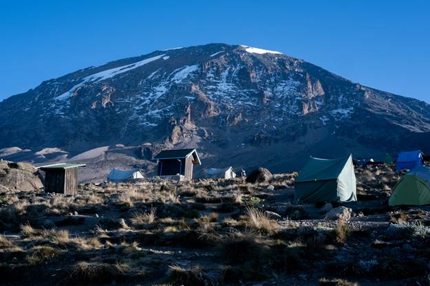 Camping tents set up below the snowcapped summit of Kilimanjaro. Trekking tourists on tour