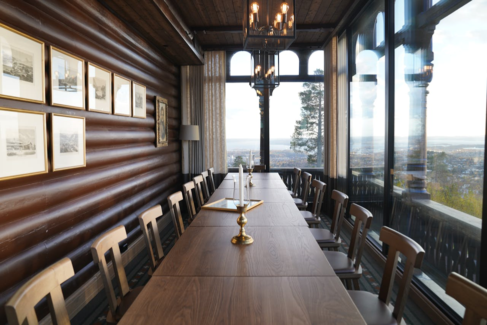 A large conference table in a hall with candle stands and glass windows, natural landscapes outside