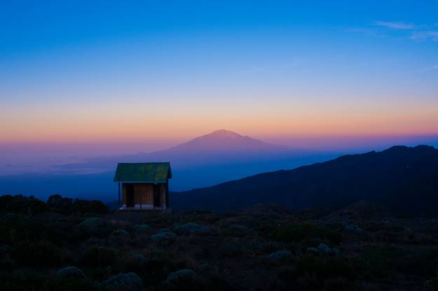 A cabin on a mountain slope with the peak ahead during golden hour. Cabin used by hikers
