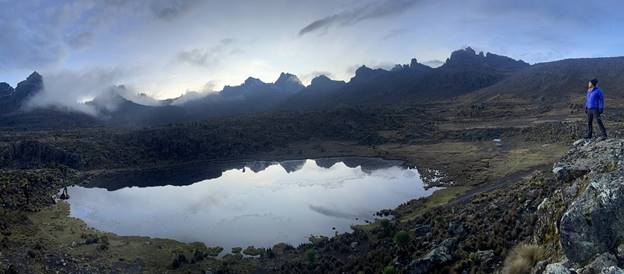 Hiker looking at a Mount Kenya lake with high peaks in the distant as the sun goes down