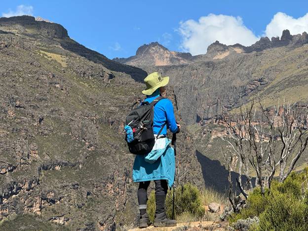 A mountain climbing woman looking at the peaks of Mt Kenya, carrying a backpack wearing a safari hat