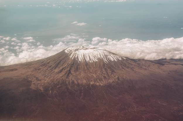 A grand aerial shot of Mount Kilimanjaro, piercing the clouds and snowcapped summit reached