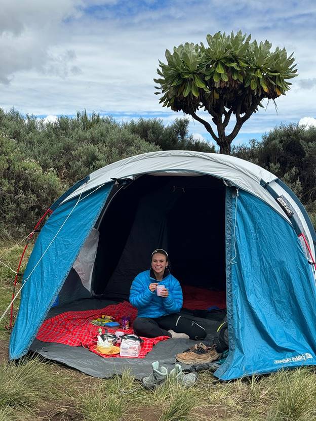 A woman on a Mount Kenya trek smiling and having lunch in her blue tent, sitting on Maasai shuka