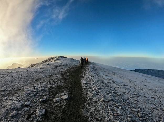 Hikers trekking on the Mount Kilimanjaro summit. Hiking trail on the snowcapped summit, clear skies.