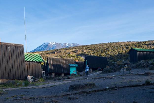 Accommodation huts on Marangu Mount Kilimanjaro trekking route. Snowcapped summit on a sunny day.