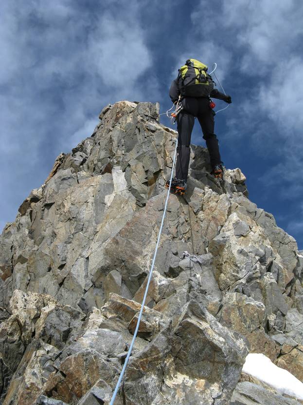 A mountain climber rock climbing Mount Kenya Batian with gear like ropes, anchors, and crampons