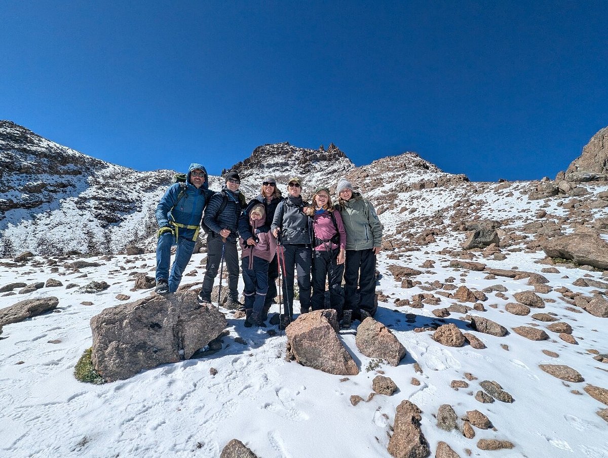 Mountain climber victory posing on Mount Kenya trek with peaks and campsite up ahead. Blue sunny sky