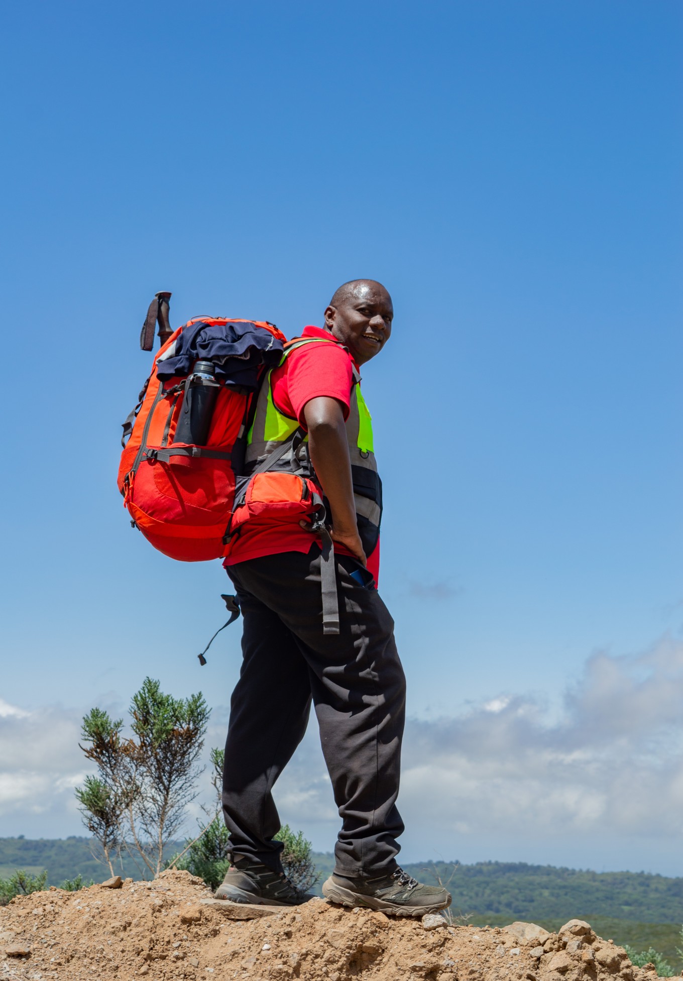 A Mount Kenya climbing guide carrying a large backpack on the slopes of the mountain on a sunny day