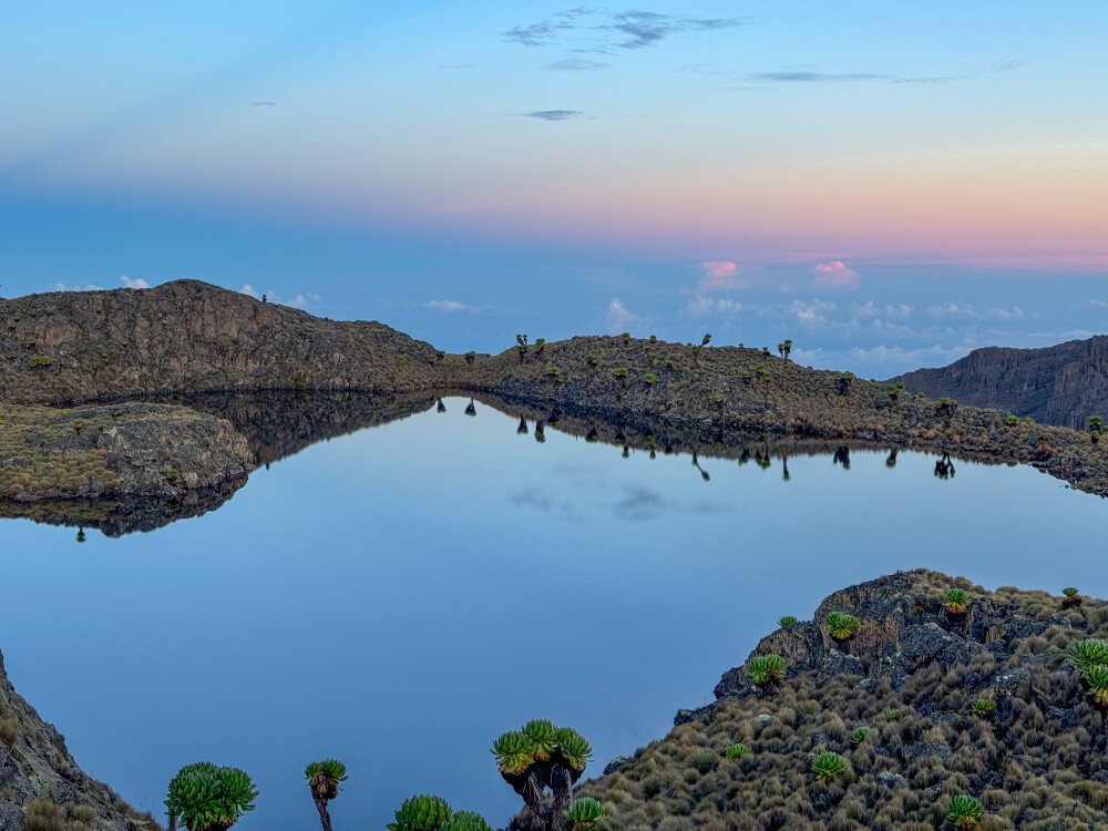 A mountain lake on Mount Kenya reflecting the blue sky with clouds in the distant below