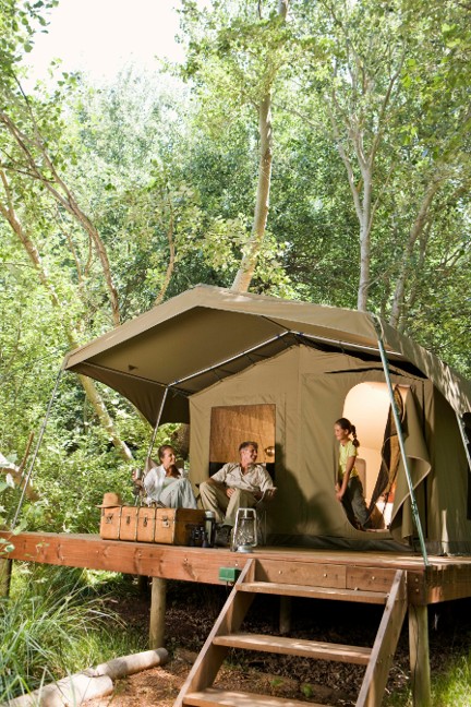 A family in a semi-permanent tented safari tent situated in the woods. Raised on wooden columns