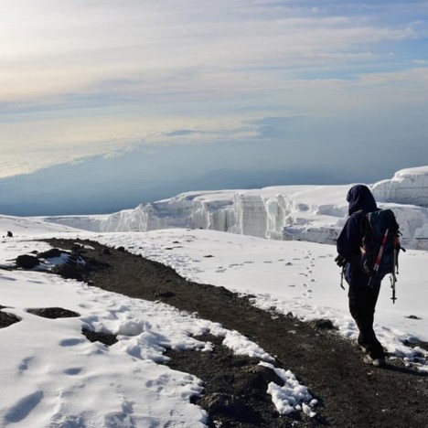 A hiker trekking Mount Kilimanjaro’s summit snowy trails with massive glaciers on his side