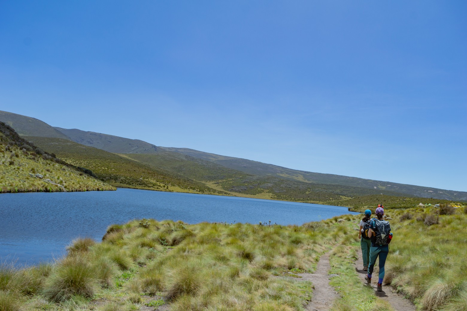 Two hikers trekking by the shores of Lake Ellis on Mount Kenya on a clear sunny day