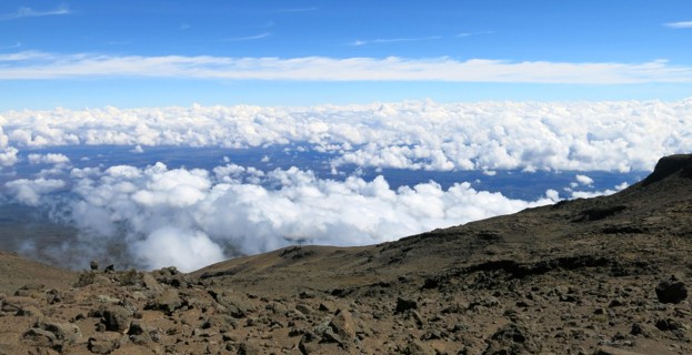 Mount Kilimanjaro landscape at high altitude on barren terrain and clouds seen below