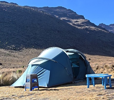 a camp set up with chairs and tables outside on the landscapes of Mt Kenya on a sunny, blue-sky day