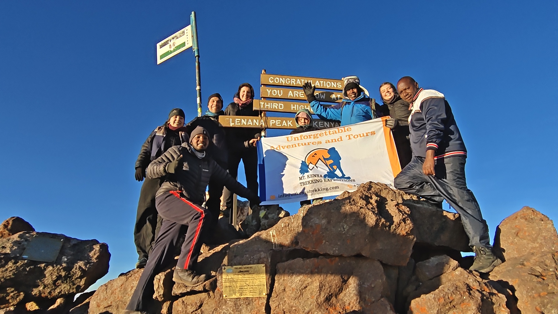 trekkers and guides posing on Pt. Lenana on a bright sunny day after successfully trekking Mt Kenya