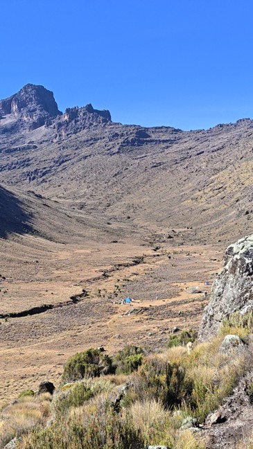 A valley on Mount Kenya with seen from a cliff with a campsite below and the peaks ahead