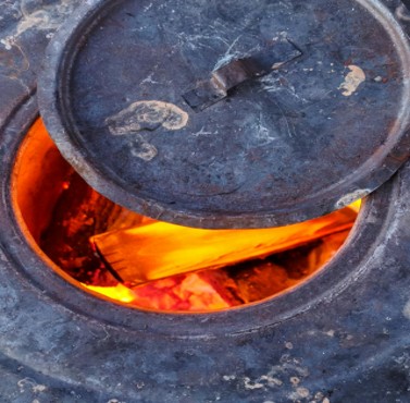 A warming stove with red hot timber inside with a lid partially open